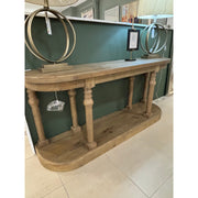 The Glenbawn Console, crafted from reclaimed wood with rounded corners and spindle legs, stands against a green wall, topped with two lamps with circular metal bases and a framed item—a timeless furniture piece.