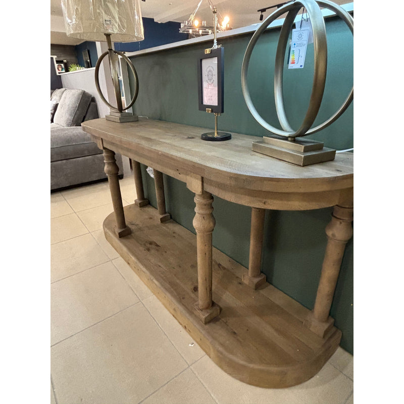 The Glenbawn Console with spindle legs and a lower shelf stands against a green wall. Two decorative lamps with circular metal bases are on top, flanking a framed picture. Beige tile flooring completes the scene.
