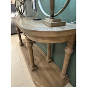 The Glenbawn Console, crafted from reclaimed wood with four spindle legs and a lower shelf, stands against a green wall. Two decorative lamps with circular bases sit on top, and light-colored tiles cover the floor.