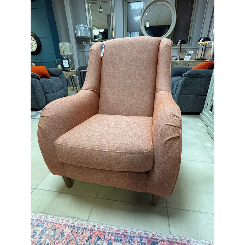 Accent chair with a high back and deep seat, featuring a warm pink-orange woven fabric and a relaxed, curved silhouette, displayed in a home goods showroom.
