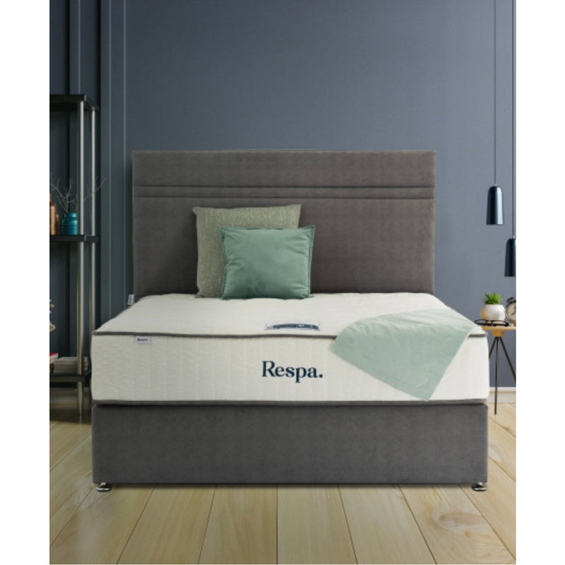 A modern bedroom with a grey upholstered bed, green and grey cushions, a Respa Ashford Mattress with Sleepfresh technology, a light green throw, minimalist decor, dark grey walls, and wooden flooring.