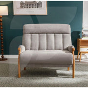 The Blaze Loveseat in modern gray light oak with wooden arms and legs sits on a patterned rug. In the background, a floor lamp, framed artwork, and a wooden side table with books stand against a teal wall.