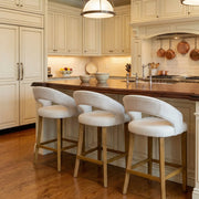 A kitchen with cream-colored cabinets, a wood island countertop, three Willow Counter Stools, hanging pendant lights, and copper pots displayed on a rack above the stove.