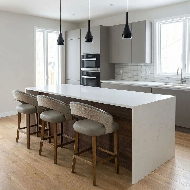 Modern kitchen featuring a large white marble island, three Willow Counter Stools, light wood floors, sleek gray cabinets, built-in ovens, white tile backsplash, and three black pendant lights above the island.