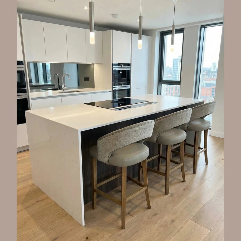 Modern kitchen with a large white island, three Willow Counter Stools, built-in appliances, white cabinets, wood flooring, pendant lights, and large windows offering a city view.