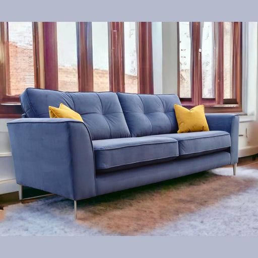 The Turino sofa by vendor-unknown, in blue aquaclean fabric, features two yellow accent pillows and rests on a light-colored rug before large wooden-framed windows. Natural light highlights the modern, cozy space and the sofa’s durable upholstery.
