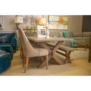 A modern living room showroom featuring the Audrey Dining Table by vendor-unknown, beige upholstered chairs, a bench, gray sectional sofa, colorful abstract paintings, and decorative items on the table.