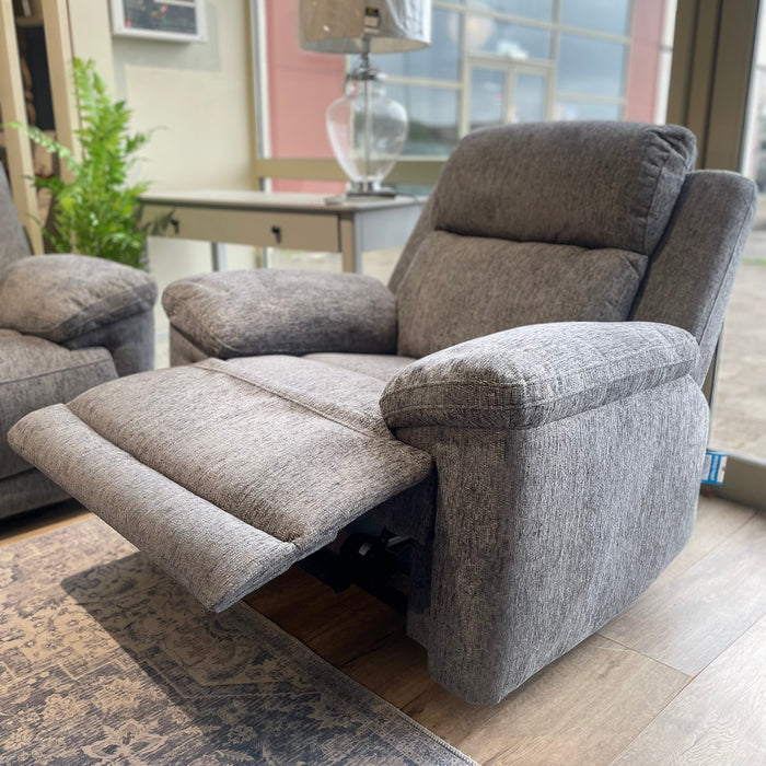 The Elenor Electric Reclining Range features a gray upholstered electric recliner with luxury fabric and footrest extended, set near a window on a patterned rug beside a matching armchair and glass lamp for contemporary style.