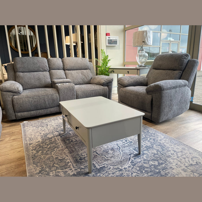 A cozy living room featuring the Elenor Electric Reclining Range in gray luxury fabric, paired with a white coffee table on a patterned rug and a lamp by large windows, seamlessly blending comfort with contemporary style.
