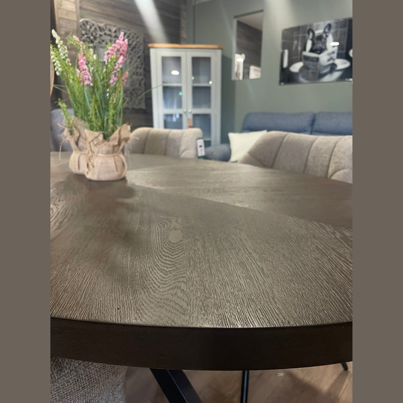 Close-up of a dark wood Samara Oval Table with a burlap-wrapped floral arrangement, surrounded by beige upholstered chairs in a cozy living room with gray walls and framed photos.