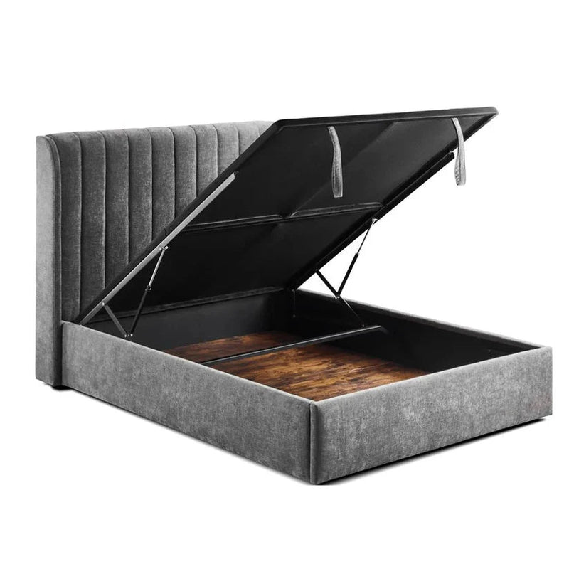 The Frida Storage Bed features grey upholstery, a tall vertical-stitched headboard, and generous under-bed storage accessible by lifting the mattress platform to reveal a spacious wooden compartment.