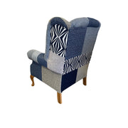 The Queen Anne Chair has wooden legs and is upholstered in blue, grey, and patterned patchwork fabric with geometric and solid designs. Shown from the back on a white background, this Irish-made chair blends classic style with modern patterns.