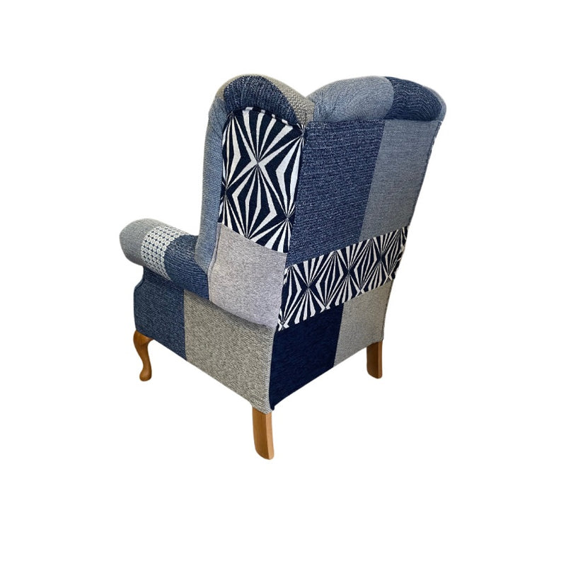 The Queen Anne Chair has wooden legs and is upholstered in blue, grey, and patterned patchwork fabric with geometric and solid designs. Shown from the back on a white background, this Irish-made chair blends classic style with modern patterns.