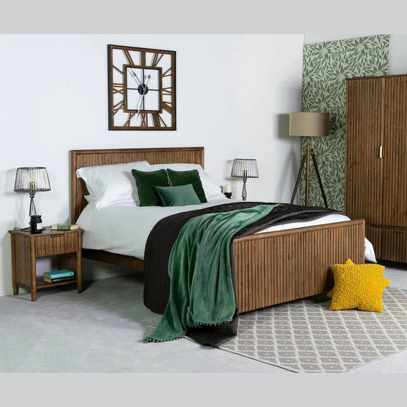 A stylish bedroom featuring rustic furniture, including the Cairo Bedframe, white bedding, green pillows, a yellow star cushion, and a gray rug. Bedside tables, lamps, a wardrobe, and a wall clock complete the inviting space.