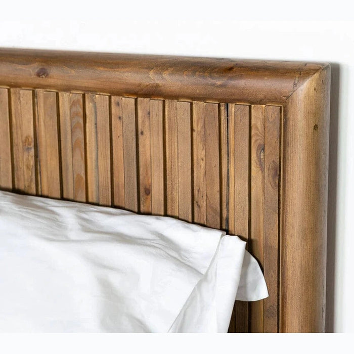 Close-up of the Cairo Bedframe's wooden headboard, featuring vertical slats and a natural finish, shown beside a bed with white linens and pillows against a plain white wall.