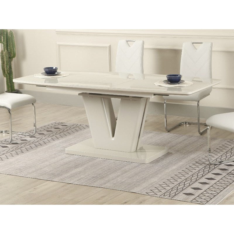 A modern dining room features the vendor-unknown Vicenza table with a V-shaped base, butterfly extension, and six cushioned white chairs with chrome legs on a patterned gray rug; two place settings are on the table.