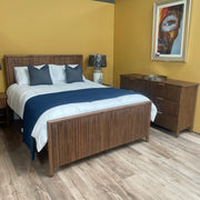 A bedroom display featuring the Cairo Bedframe with white bedding and a dark blue throw, matching nightstand and dresser, two table lamps, a colorful face painting on a yellow wall, and wood-style flooring.