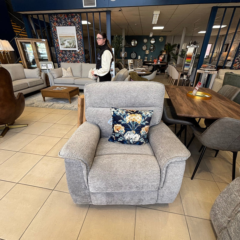 A Barrington Electric Recliner with supportive cushioning and a floral cushion is displayed in a furniture store. A woman stands among the tables and chairs, and the Mc Ginleys Furniture sign appears above.