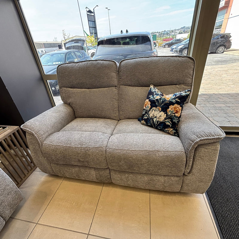 A Barrington Electric Recliner with supportive cushioning and a single floral-patterned throw pillow sits near large windows in a showroom with cars visible outside.
