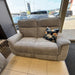 A Barrington Electric Recliner with supportive cushioning and a single floral-patterned throw pillow sits near large windows in a showroom with cars visible outside.