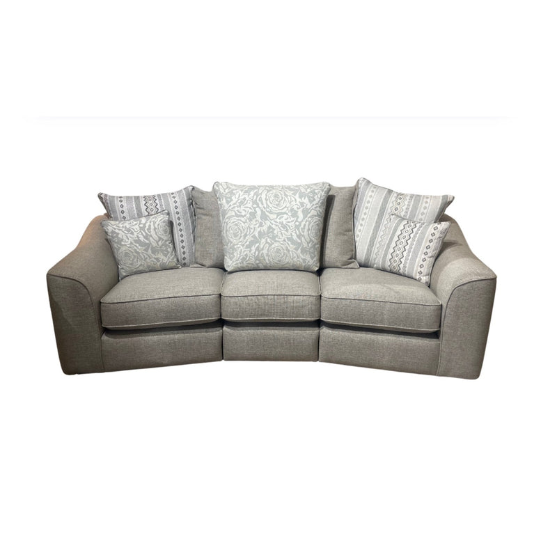 The Shelly Angle Seatee is a light gray 4-seater sofa in smooth aquaclean fabric, featuring three patterned throw pillows and two smaller accent pillows with a white background.