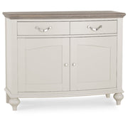 The Montreux Small Sideboard features a light gray washed oak finish, dark wood top, two drawers with metal handles, two lower cabinet doors with round knobs, and stands on four short legs.