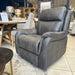 The Logan Recliner, in gray leather with visible stitching and cushioned armrests, is showcased in a furniture showroom beside a comfy sofa, tables, chairs, and other home décor.