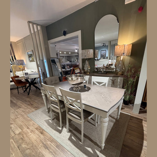 A dining room featuring the Montreux Range 180cm-225cm Set, wooden and leather chairs, a large mirror, two lamps on a sideboard, wood flooring, a beige rug, and green walls with decorative accents.
