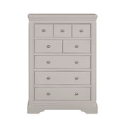 The Lima Tall Chest, in light gray with a modern design, features seven drawers of varying sizes, each with a round silver knob—an ideal addition to any taupe bedroom collection.