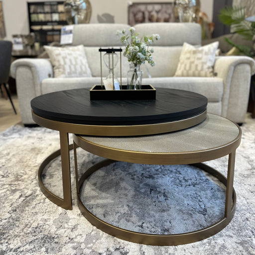 A modern living room features a light gray sofa, two round Noir Coffee Table Nest with gold frames, a vase with flowers, a lantern, and two silver lamps behind the sofa.