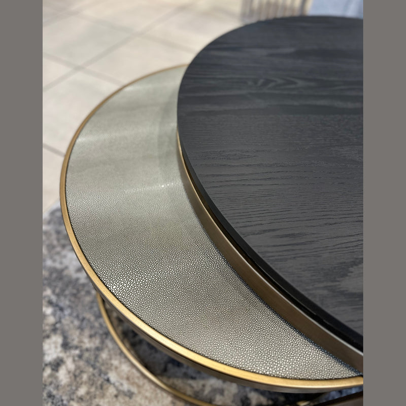 Close-up of the Noir Coffee Table Nest: one table has a textured light metallic top, the other a smooth dark wood surface; both feature gold-colored rims and rest on a gray carpeted floor.