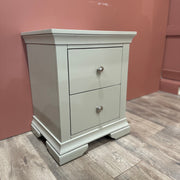 The Malmo Locker, a light gray bedside table with two drawers and silver knobs, provides durable storage on wood flooring against a muted pink wall.