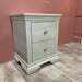 The Malmo Locker, a light gray bedside table with two drawers and silver knobs, provides durable storage on wood flooring against a muted pink wall.