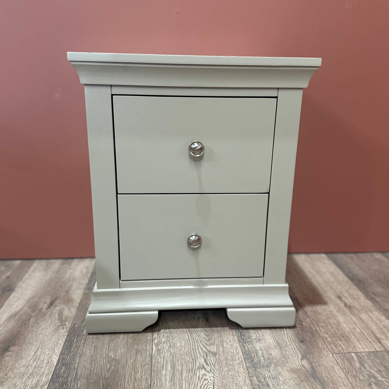 A light gray Malmo Locker with two drawers and silver knobs stands on a wood floor against a muted pink wall, providing a durable storage solution.