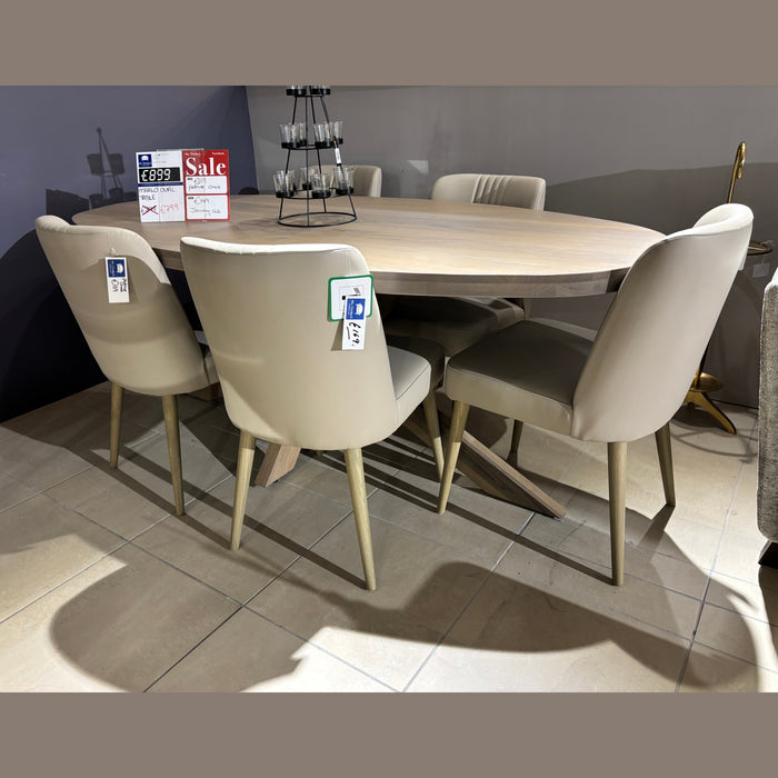 A round wooden dining table with six Patrice Dining Chairs in taupe leather is displayed in a showroom with sale signs and price tags on the contemporary set, atop tiled flooring.