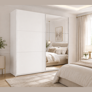 A modern bedroom with neutral tones, featuring the Vigo Sliderobe—a large white wardrobe with mirrored sliding doors—alongside a beige upholstered bed, a light wood nightstand, and soft natural light filtering through sheer curtains.