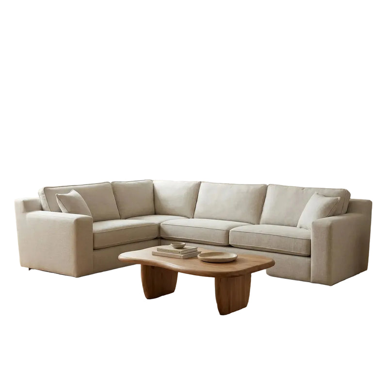 A modern living room featuring the Alice Corner Group in beige aqua clean fabric, a wooden coffee table, jute rug, large potted plant, arched windows, minimalist decor on a floating shelf, and a neutral-toned wall.