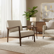A modern living room with the Monza Armchair in linen fabric and walnut armrests, a matching sofa, wooden side table with lamp, geometric rug, potted plant, abstract wall art, and light streaming through sheer curtains.