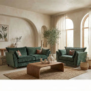 An elegant living room featuring a Cleo Range sofa, wooden coffee table, woven rug, sheer curtains on arched windows, a potted tree, and minimalistic wall art.