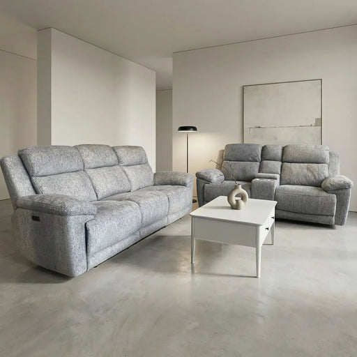 A modern living room features the Elenor Electric Reclining Range in gray chenille fabric, a matching armchair, a white coffee table with ceramic vases, a floor lamp, and abstract wall art. Light walls and a concrete floor complete the contemporary look.