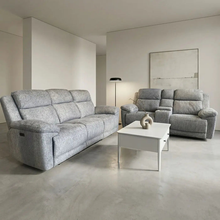 A modern living room features the Elenor Electric Reclining Range in gray chenille fabric, a matching armchair, a white coffee table with ceramic vases, a floor lamp, and abstract wall art. Light walls and a concrete floor complete the contemporary look.