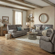 A cozy living room features the Gibson Electric Recliner in gray, a round coffee table, decorative pillows, a large round mirror on the wall, wooden ceiling beams, and sunlight streaming through beige-curtained windows.