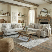 A cozy living room with two Monroe Sofa Range pieces in light gray Aqua Clean fabric, a wooden coffee table, woven pouf, patterned rug, and stone fireplace. The space highlights neutral tones, natural light, and rustic decor.