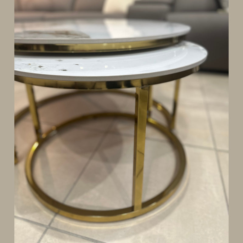 Two Kas Nest - Gold Base round modern nesting coffee tables with white marble tops and gold frames sit on a tiled floor in front of a dark gray sofa with light-colored cushions.