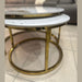 Two Kas Nest - Gold Base round modern nesting coffee tables with white marble tops and gold frames sit on a tiled floor in front of a dark gray sofa with light-colored cushions.