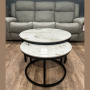 The Kas Nest set features two round modern nesting coffee tables with white marble tops and black metal frames, shown on a wood floor in front of a gray upholstered sofa.