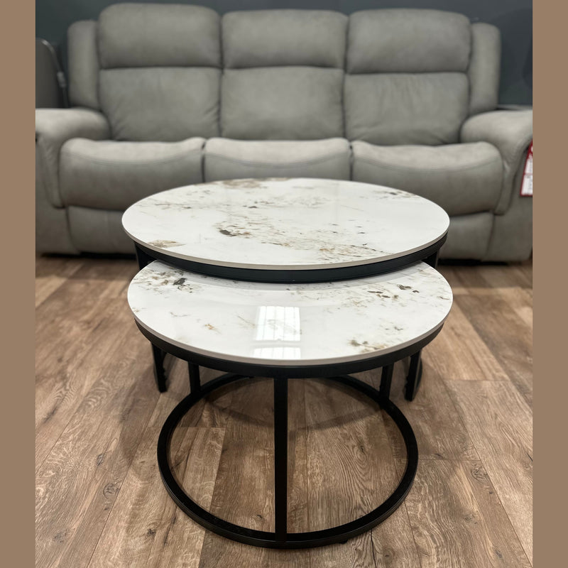 The Kas Nest set features two round modern nesting coffee tables with white marble tops and black metal frames, shown on a wood floor in front of a gray upholstered sofa.