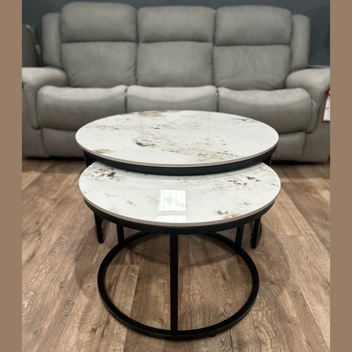 The Kas Nest set features two round modern nesting coffee tables with white marble tops and black metal frames, shown on a wood floor in front of a gray upholstered sofa.