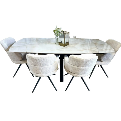 The Positano Table with a glossy sintered stone top is paired with 6 Orbit light gray upholstered chairs with black legs. The table is styled with a floral vase and a decorative glass lantern.