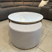 The Vienna Coffee Table + Footstool features a marble top with gold accents and a light gray upholstered ottoman beneath, placed in front of a modern dark gray sectional on tiled floors.